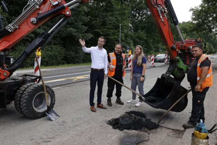 Stadtkämmerer und Dezernent Martin Wilhelm und Melanie Gessner beim Besuch der Bauarbeiten auf der Seligenstädter Straße. Vorarbeiter Salim Saroukh (Mitte) erläutert, wie aus einer Ladung Asphalt eine glatte Fahrbahn wird. Foto: Stadtwerke Offenbach/Bernd Georg